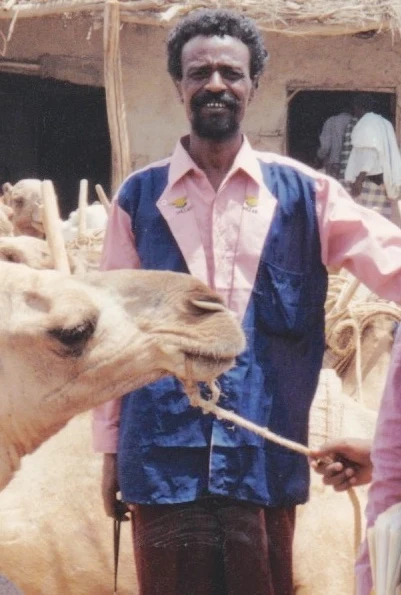 An Afar storyteller stands behind a camel in a camel market