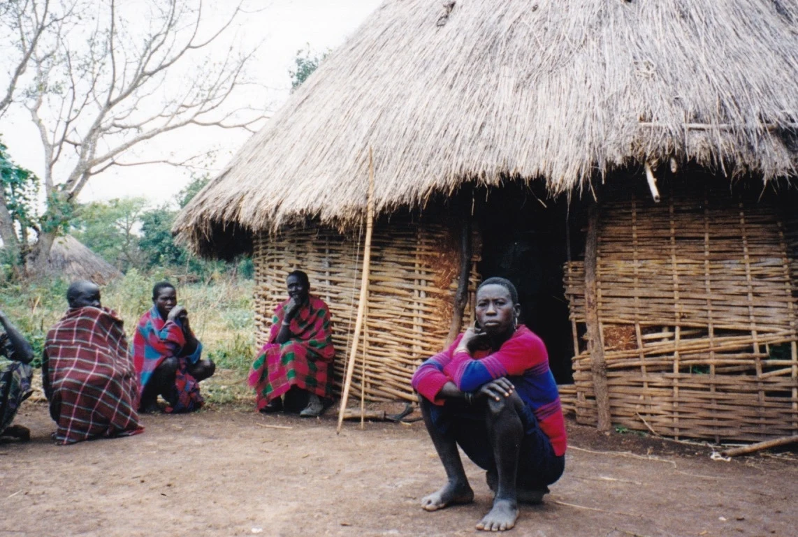 Gumuz storytellers sit outside a round woven house with a thatched roof