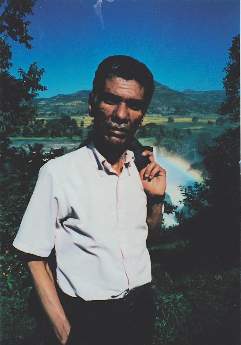 Mesfin Habtemariam stands beside water with hills behind him