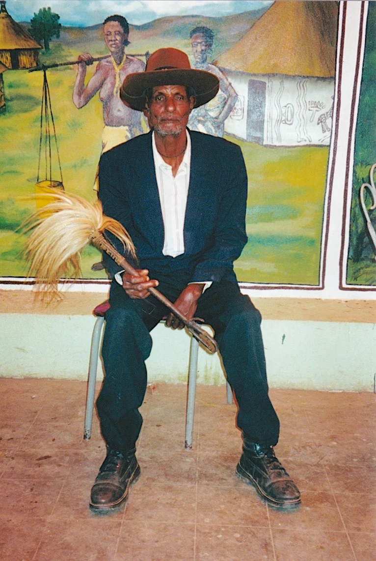 Shirguma Soraga seated with a Stetson and flywhisk during a storytelling session