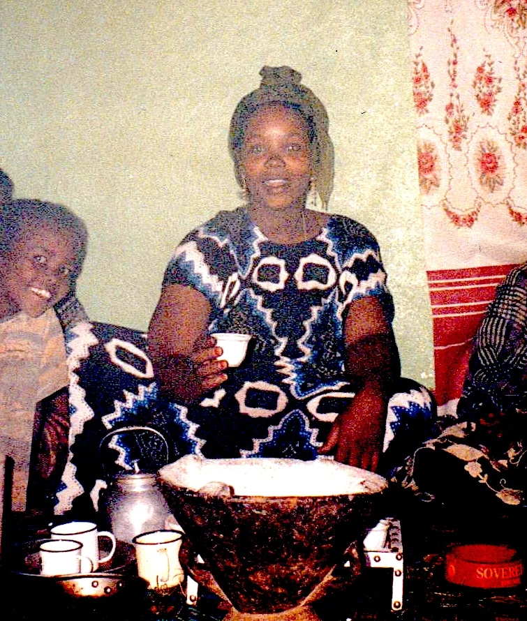 Fatuma Omer sits inside her house holding a coffee cup, with a coffee pot and cups before her
