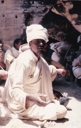 A Tigrayan priest in white robes and a white turban seated against a rock face